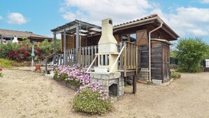 Un chalet rustique avec une cheminée en pierre, une terrasse en bois et un jardin agrémenté de fleurs roses.