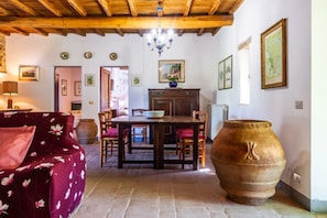 A room with a wooden ceiling, a dining table with chairs, a large vase, and a sofa with floral upholstery.
