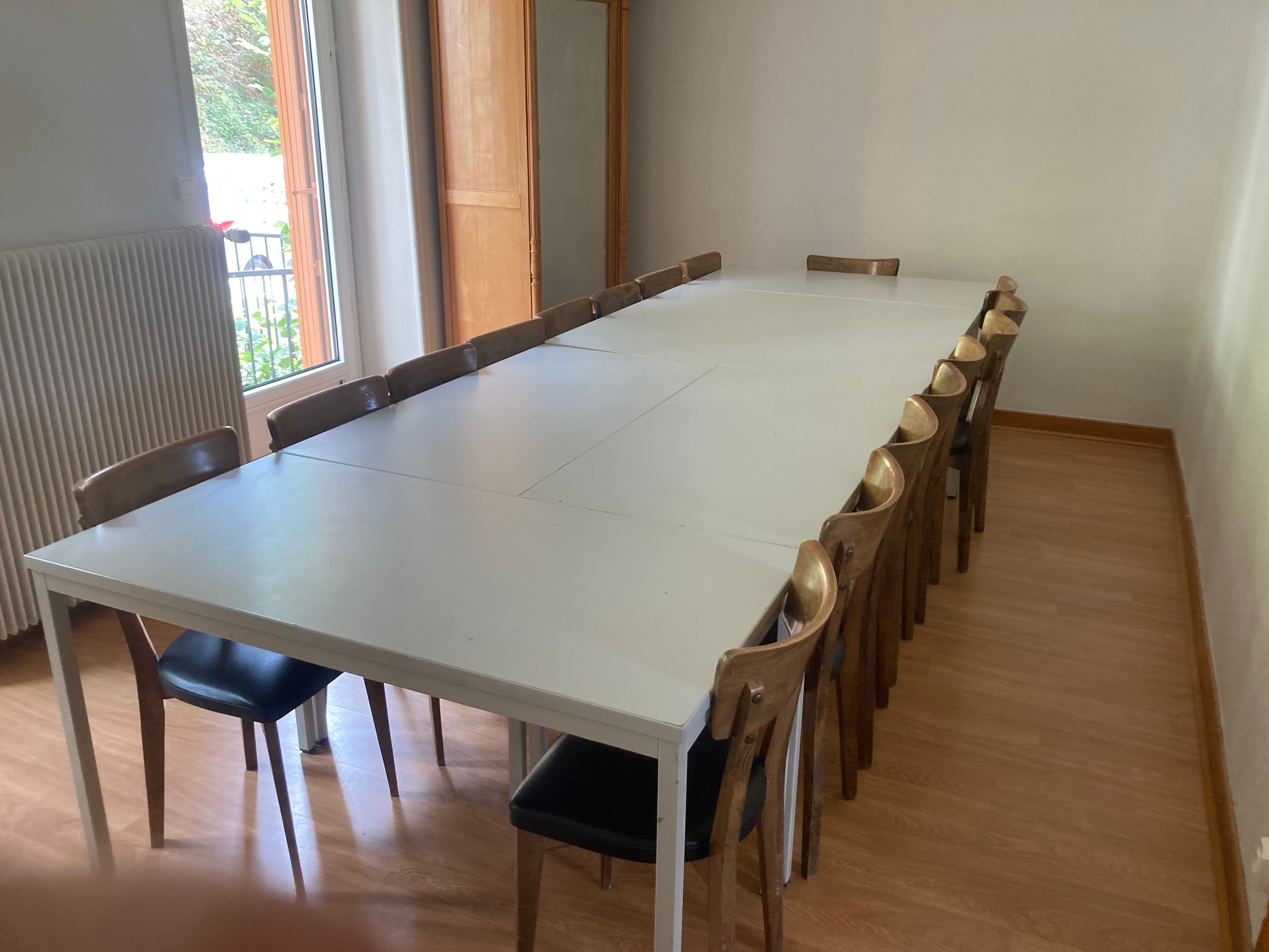 Uma sala de conferências com uma mesa comprida e cadeiras, um radiador e uma janela com vista para o verde.