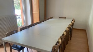 A conference room with a long table and chairs, a radiator, and a window with a view of greenery.