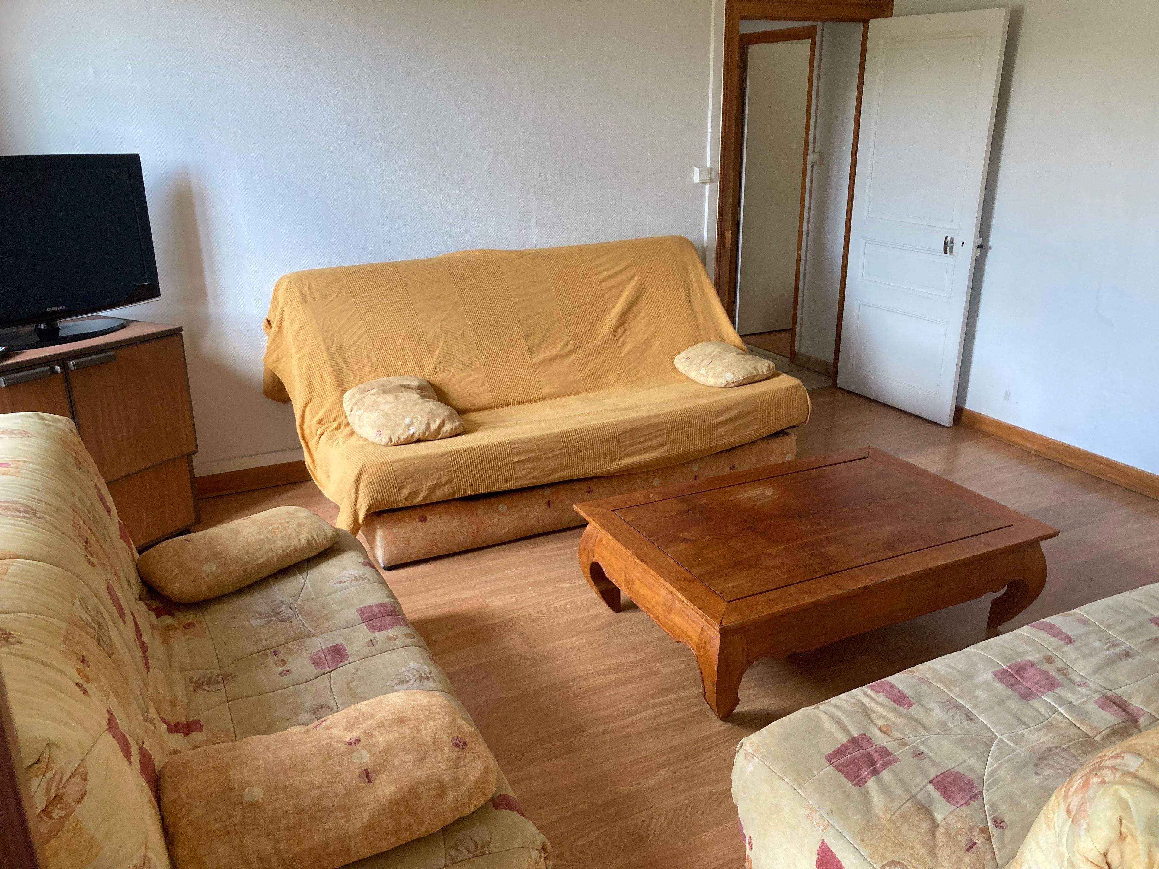 Een woonkamer met een bank, een houten salontafel en een televisie op een kast.