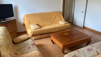 Een woonkamer met een bank, een houten salontafel en een televisie op een kast.