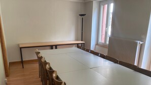 Un salón de conferencias con una larga mesa y sillas, una lámpara de pie y una ventana con persianas.