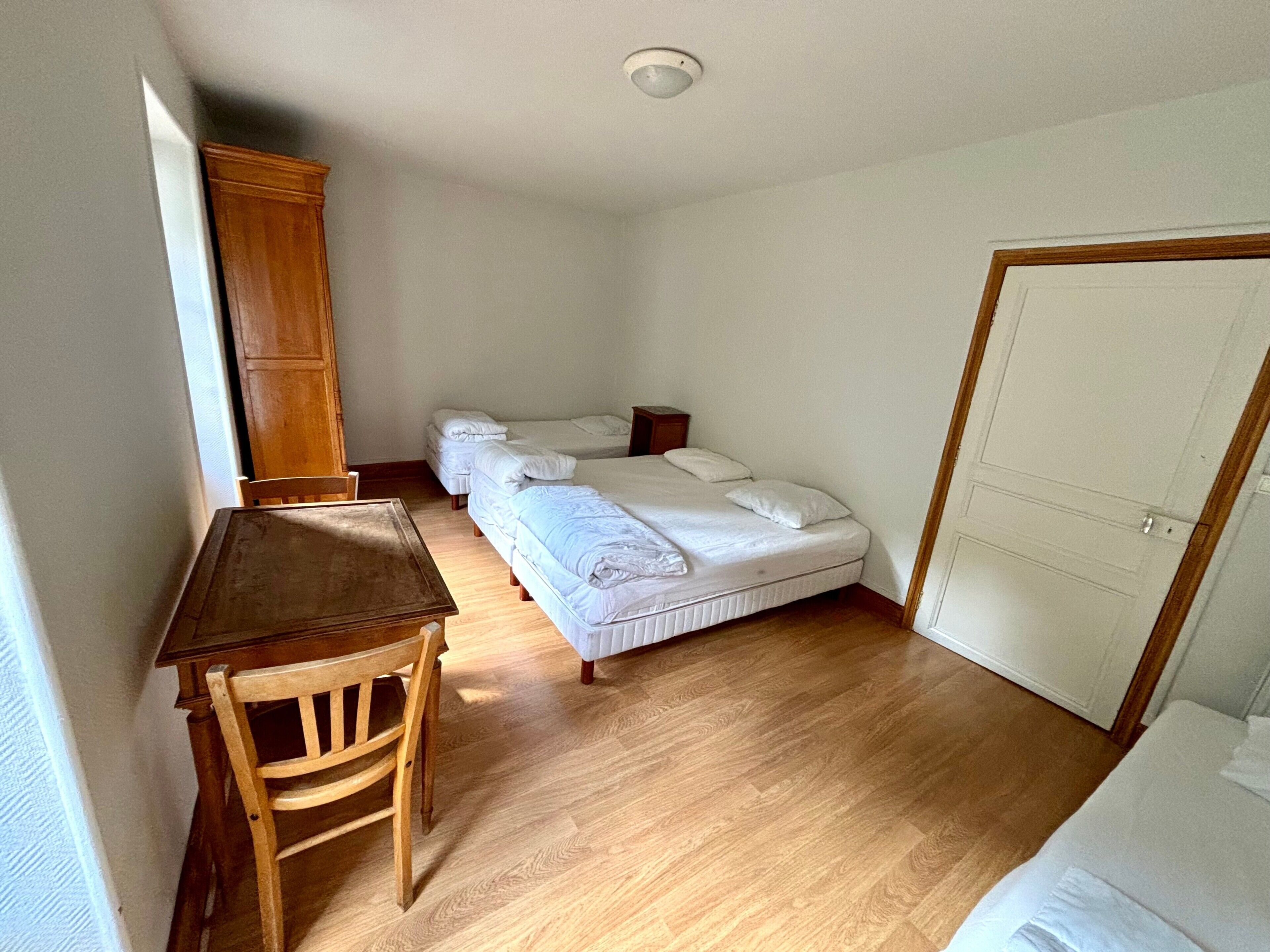 Quarto com escrivaninha de madeira, duas camas de solteiro, guarda-roupa e uma porta.