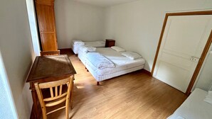 Una habitación con escritorio de madera, dos camas individuales, un armario y una puerta.