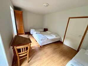 Une chambre avec un bureau en bois, deux lits simples, une armoire et une porte.