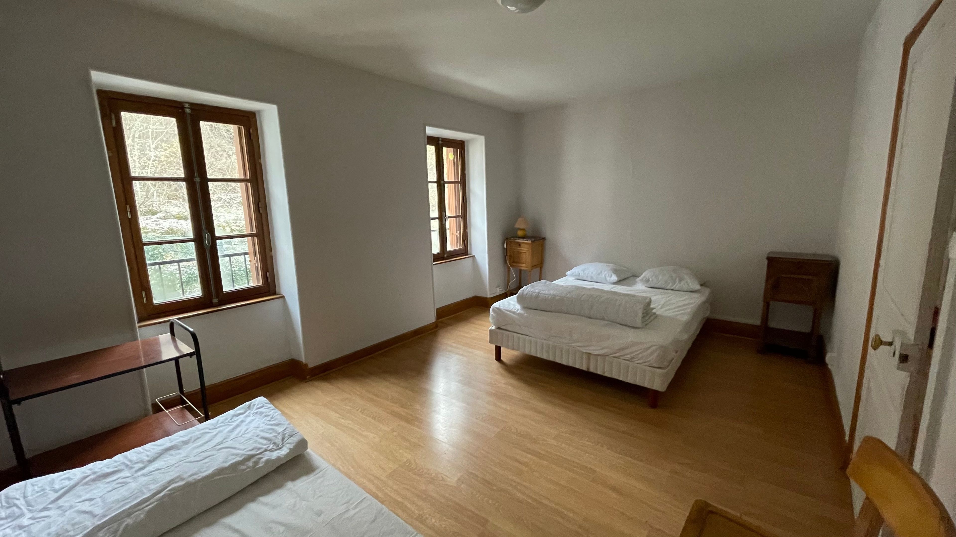 Une chambre à coucher avec un lit, une table de chevet, un plancher en bois et deux fenêtres.