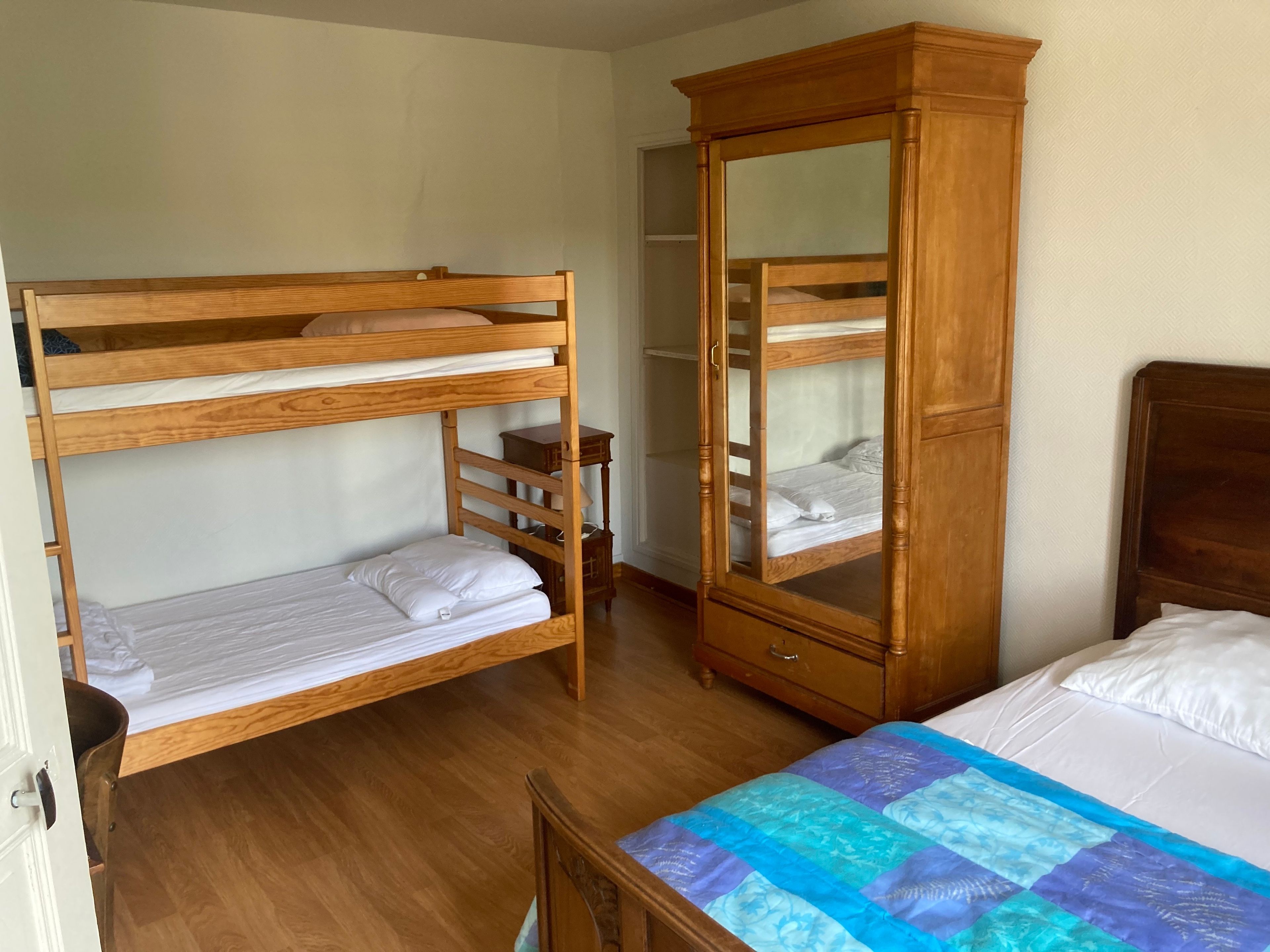 A room with a bunk bed, a wardrobe, and a bed with a quilt.