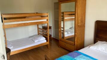 A room with a bunk bed, a wardrobe, and a bed with a quilt.