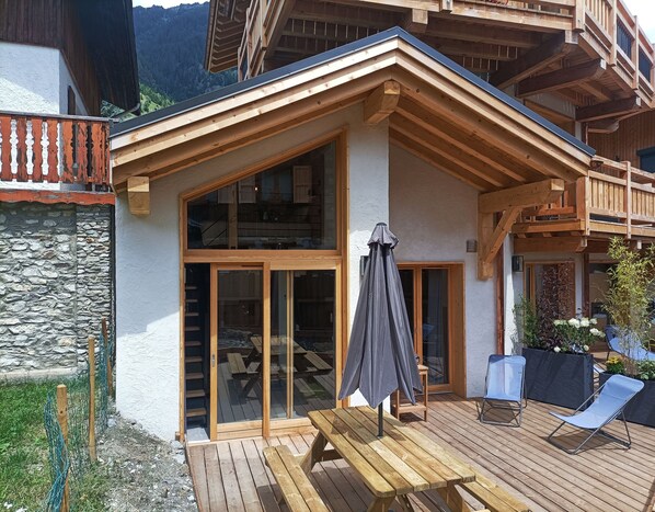 A wooden chalet with a balcony, a wooden deck, and a stone wall.