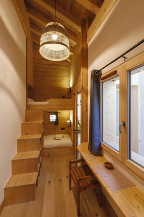 Interior de madeira com uma cama beliche, uma escrivaninha e uma janela com cortinas.