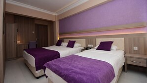 Habitación de hotel con dos camas, un armario de madera y una pared de acento morada.