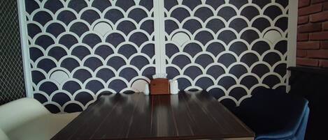 A dining area with a table and chairs, a decorative wall with a scalloped pattern, and a brick wall in the background.