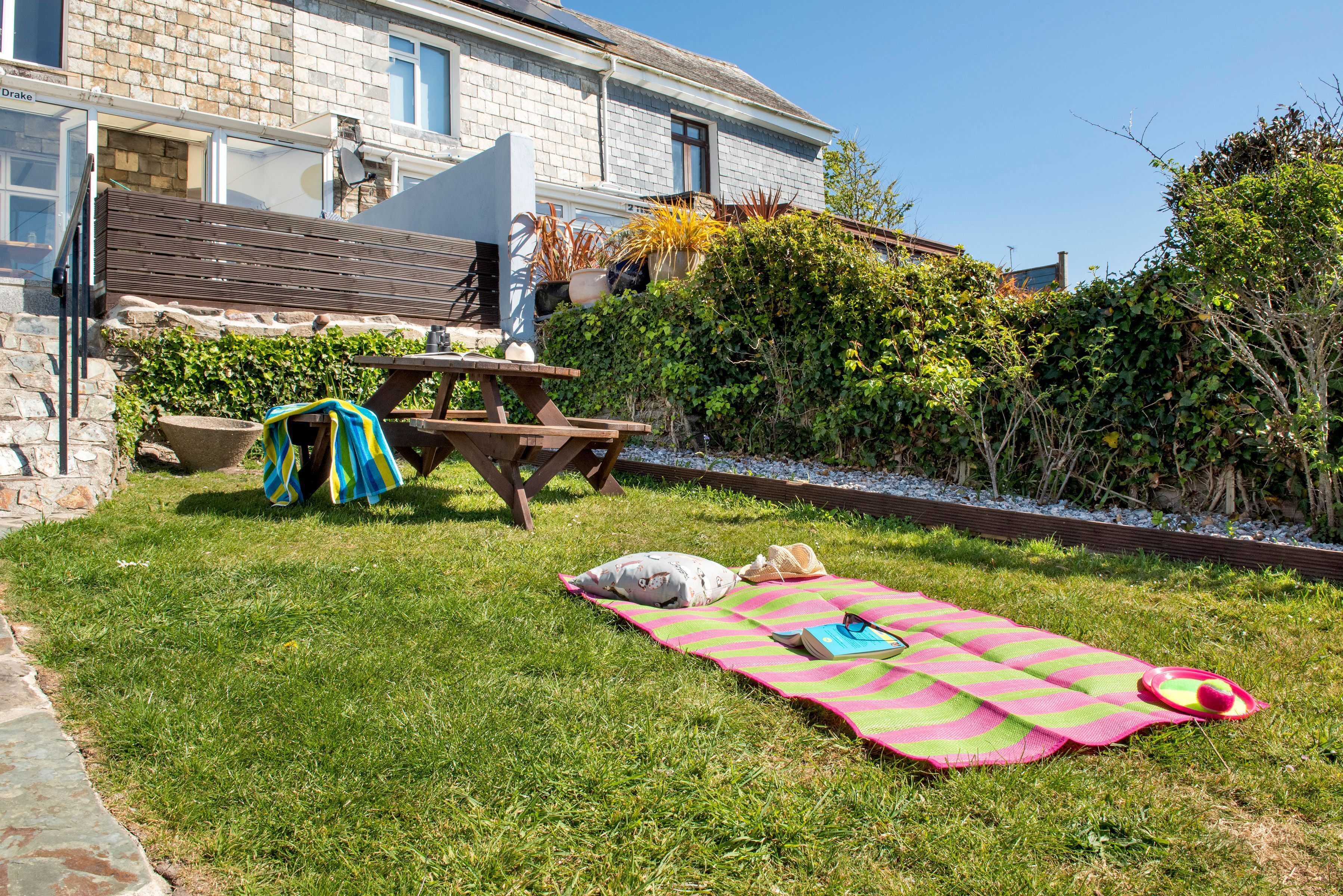 A grassy backyard with a picnic table, a blanket, and outdoor furniture.