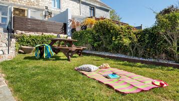 A grassy backyard with a picnic table, a blanket, and outdoor furniture.