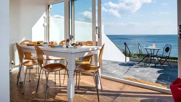 Un comedor con mesa y sillas, vista al mar y un patio con mesa y sillas.