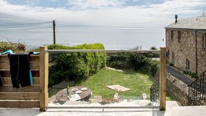 Une vue depuis un balcon donnant sur une cour verdoyante, avec un bâtiment en pierre, une clôture en bois et une table avec des sièges pour l’extérieur.