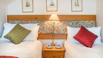 A double bed with a wooden headboard, two pillows, a nightstand with a lamp, and two cups.