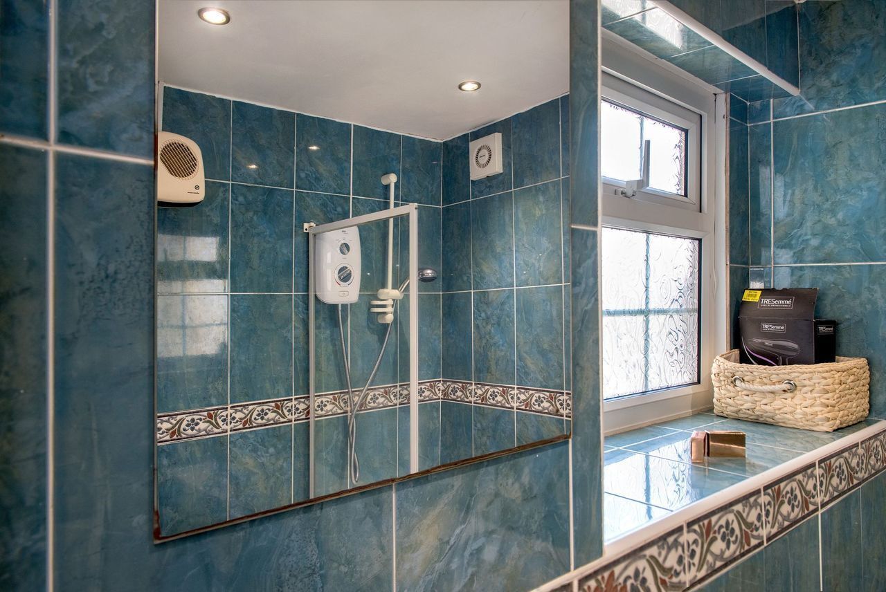 A bathroom with blue tiles, a shower, a large mirror, and a window.
