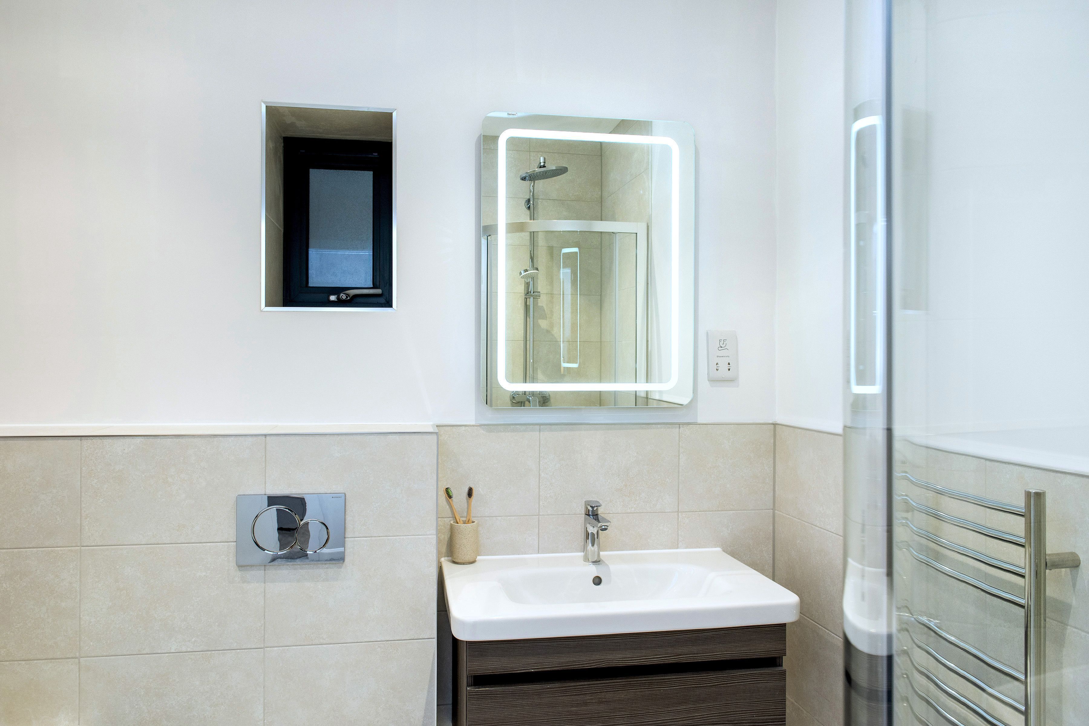 Un baño moderno con ducha integrada, lavamanos con espejo y toallero.