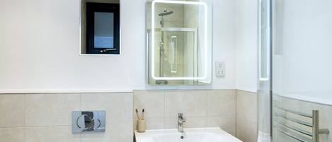 Un baño moderno con ducha integrada, lavamanos con espejo y toallero.