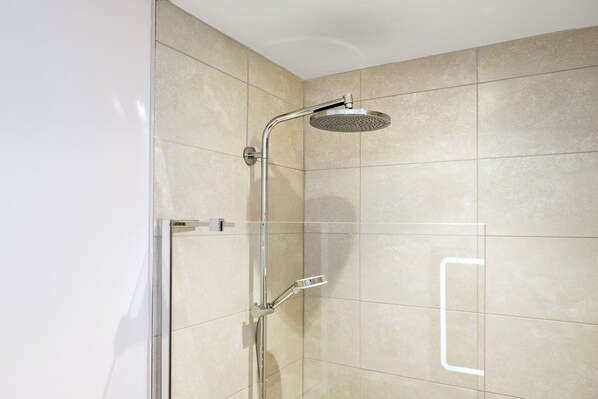 A shower with a handheld showerhead and a wall-mounted control panel.