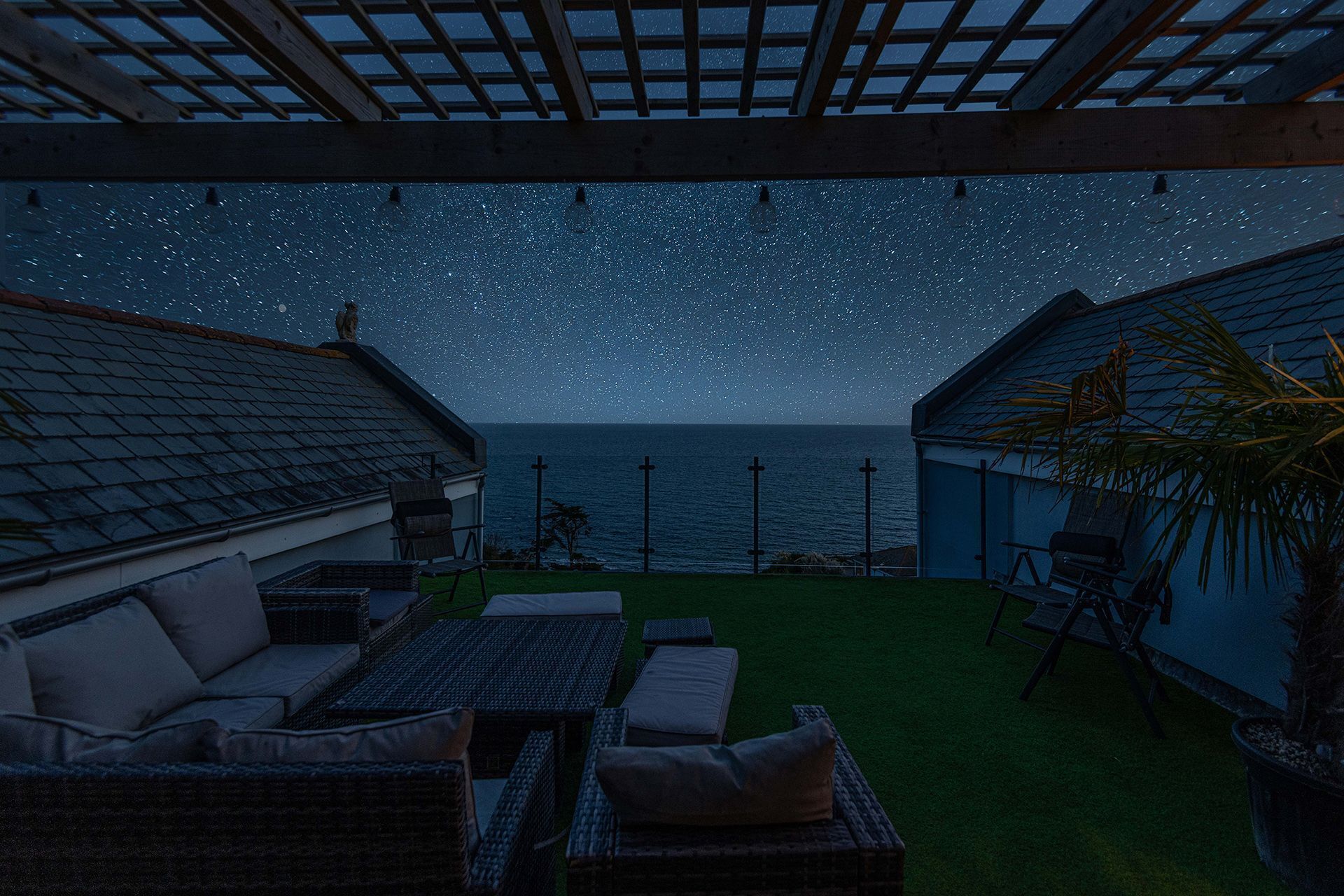 A covered outdoor area with a starry night sky, a view of the sea, and outdoor furniture.