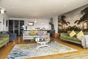 A modern living room with a sofa, a coffee table, and a painting of trees on the wall.