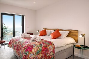 Une chambre avec un grand lit, une tête de lit en bois et une vue sur l’extérieur.