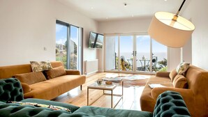 A modern living room with a sofa, a coffee table, and a view of the outdoors. - Turnstone -  Beach-side House with Terrace Hot Tub & Stunning Views (Portwrinkle)