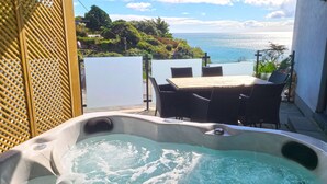 Un bain à remous avec vue sur l’océan, une table en bois et des chaises.