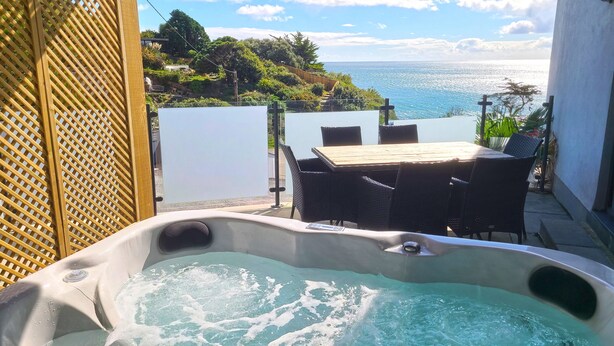 A hot tub with a view of the ocean, a wooden table, and chairs. - Turnstone -  Beach-side House with Terrace Hot Tub & Stunning Views (Portwrinkle)