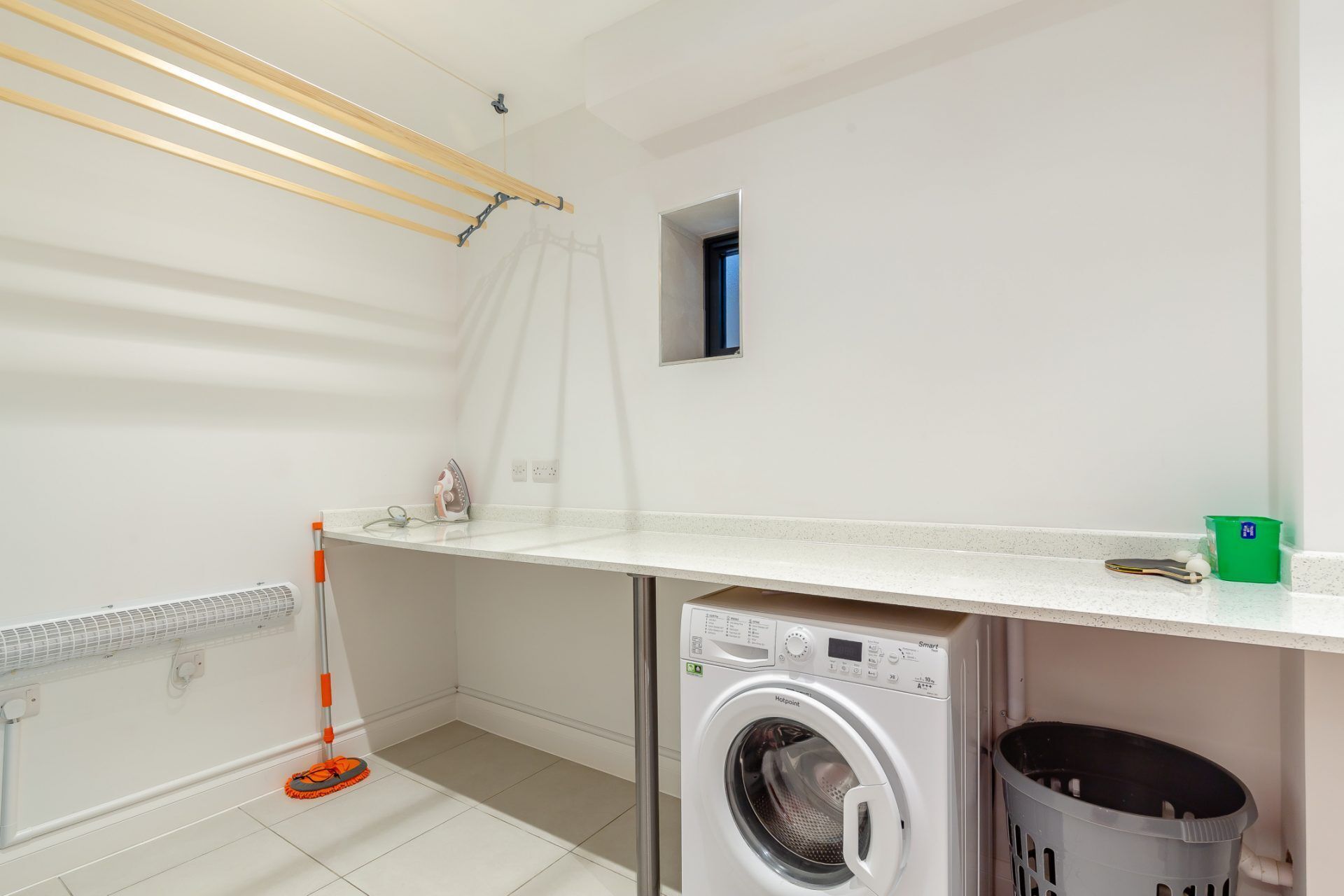 A laundry room with a washing machine, a drying rack, a broom, and a laundry basket.