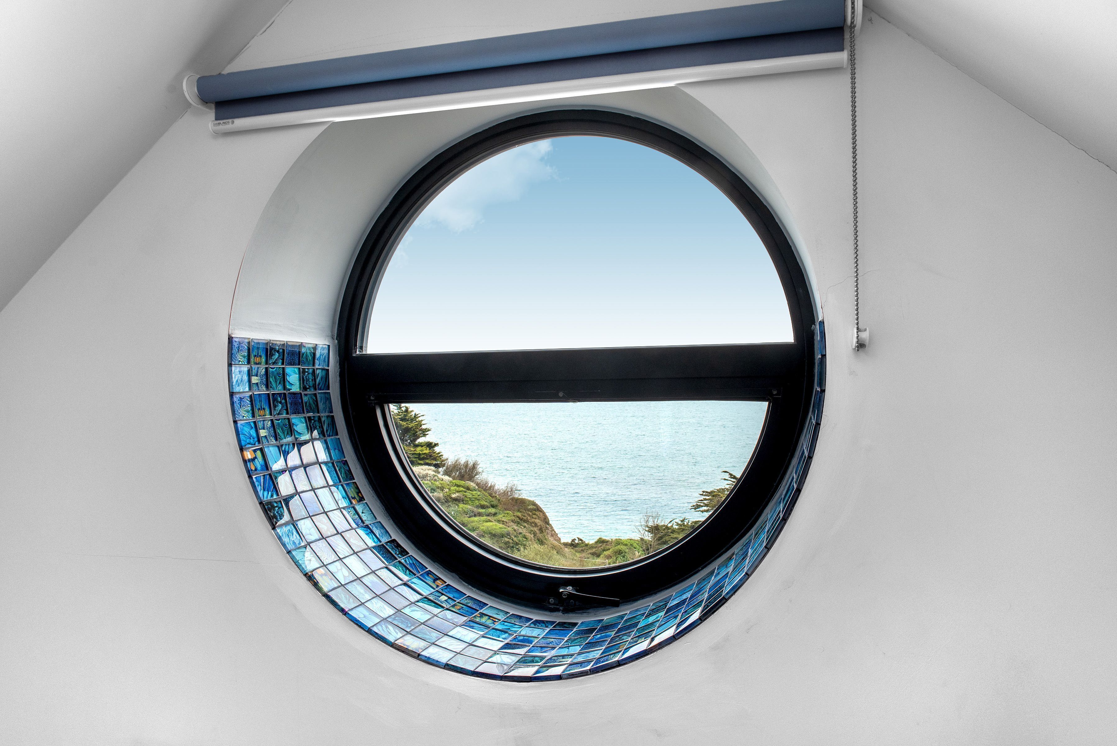 A circular window with a view of the sea and cliffs.