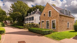 Una calle residencial con casas, incluyendo una casa de piedra con techo inclinado y una casa blanca con contraventanas.
