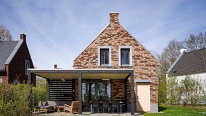 Una casa moderna con fachada de ladrillo, un porche cubierto con mobiliario exterior y un césped bien cuidado.