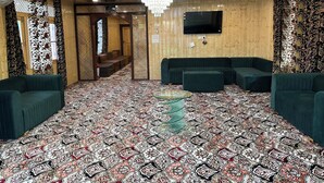 A room with a patterned carpet, green sofas, a chandelier, and a television on the wall. - The Heritage Safina Group Of Houseboats (Srinagar)