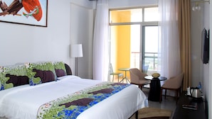 Habitación de hotel con una cama grande, un cuadro en la pared, un balcón con vistas y una pequeña mesa con sillas.