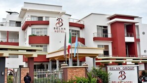 Un hotel Belan moderno con un llamativo letrero que dice 'Belan Hotel', una entrada con portones y un asta con varias banderas.