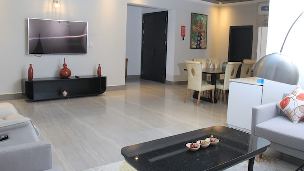 Una sala moderna con una televisión de pantalla plana, una mesa de centro negra con aderezos, un sofá blanco y un área de comedor con sillas y una mesa.