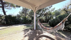 Eine Holzterrasse mit einer Hängematte unter einer weißen Pergola, umgeben von viel Grün.