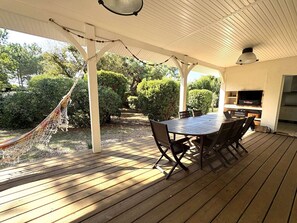 Eine überdachte Terrasse mit Holztisch und -stühlen, einer Hängematte und Blick auf den Garten sowie den Küchenbereich.