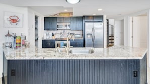 Une cuisine moderne avec des meubles de couleur sombre, un réfrigérateur en acier inoxydable et un plan de travail en granit.