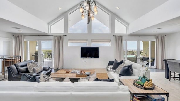 Un salon spacieux avec un plafond haut, un grand téléviseur et un coin repas comprenant une table et des chaises.