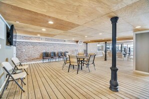 A spacious indoor area with a wooden floor, brick walls, and a ceiling with wooden panels. There are several chairs and a table in the center.
