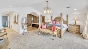 Une chambre spacieuse avec un grand lit, une coiffeuse avec un miroir et un lustre.