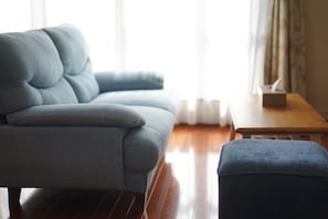 Un salon comprenant un canapé et un pouf, un plancher en bois et une petite table avec un coffre.