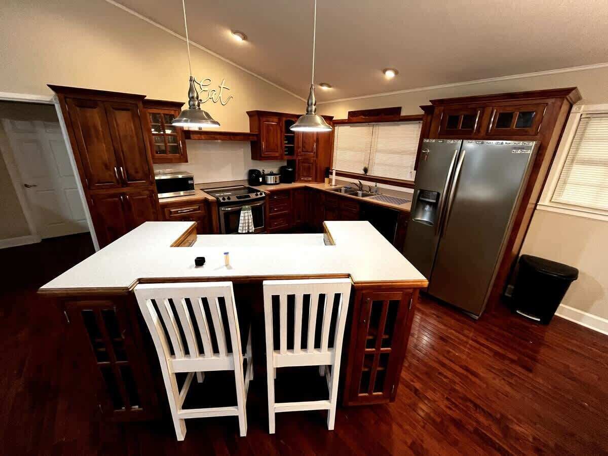Una cocina con armarios de madera, una isla grande con dos sillas, un refrigerador de acero inoxidable e iluminación colgante.