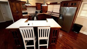 A kitchen with wooden cabinets, a large island with two chairs, a stainless steel refrigerator, and pendant lighting. - KunTree Retreat by Beyond Expectations: Pet-Friendly w/ Hot Tub, Sauna & Firepit (Sevierville)