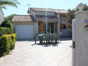 A residential property with a tiled patio, a dining area with outdoor furniture, and a garage.